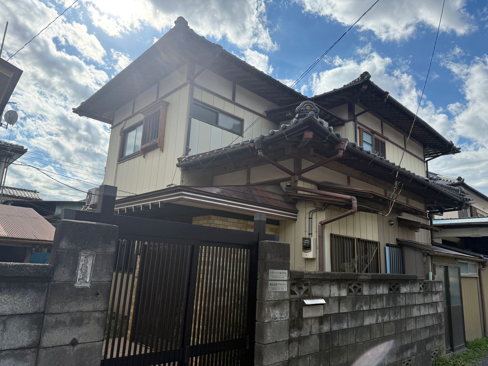 瓦屋根の 2 階建ての建物と、ブロック塀の間にある黒い門
